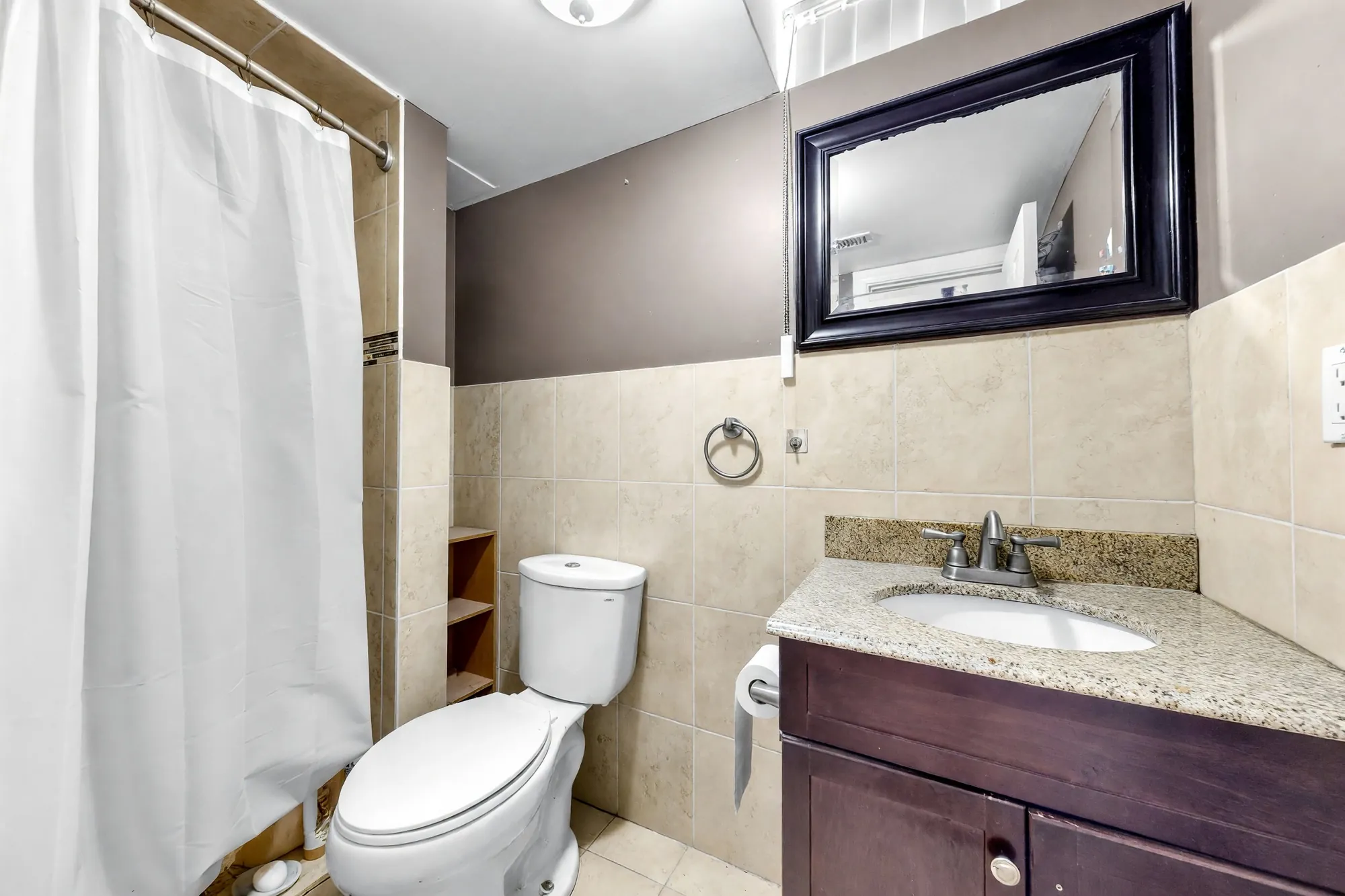 The lower-floor bathroom shown cleared: a shower curtain at the left, the toilet, a dark vanity with a granite top, a mirror