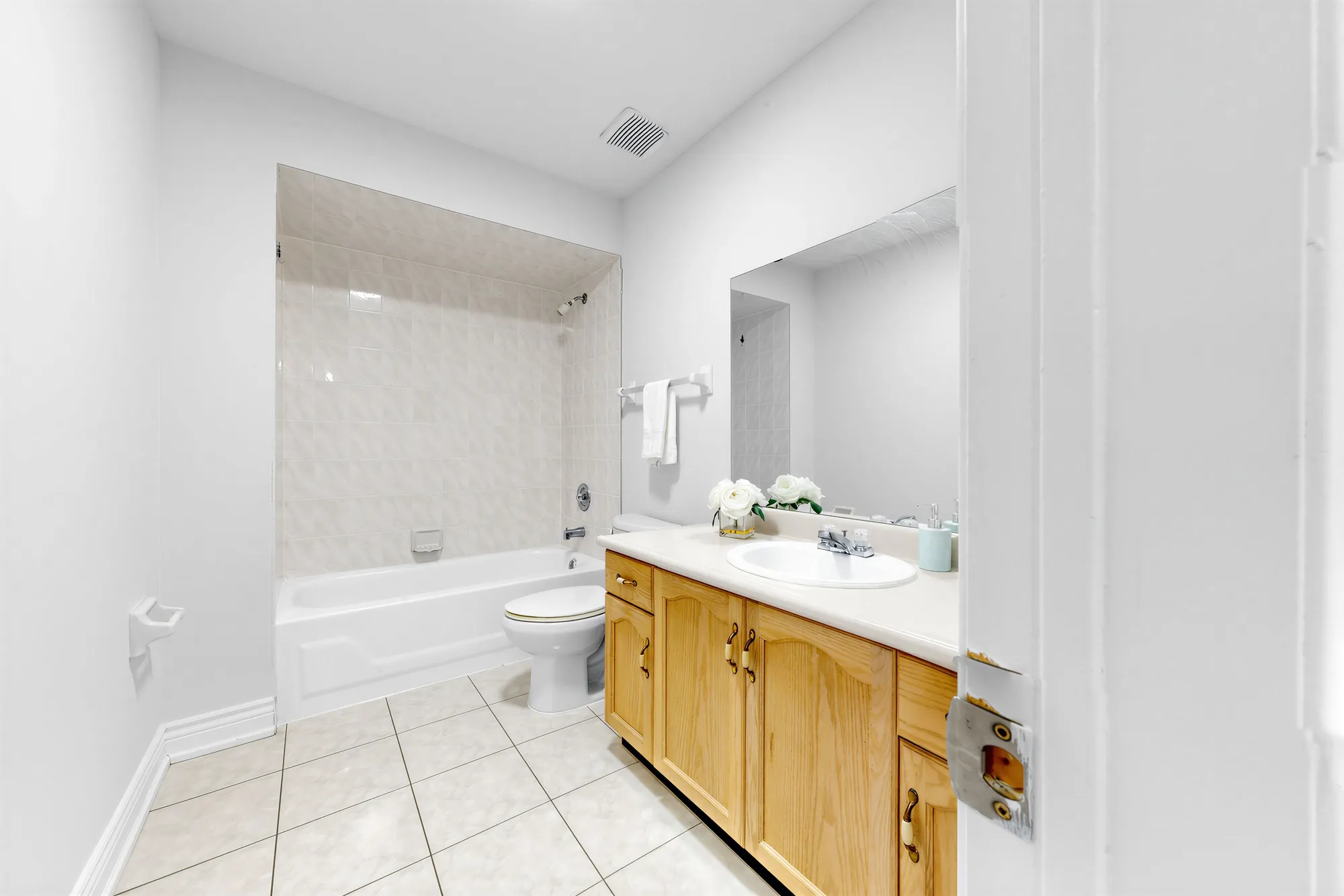 The main bathroom: a tub with a tiled surround, a maple vanity with a white top and a wide mirror, tile floor