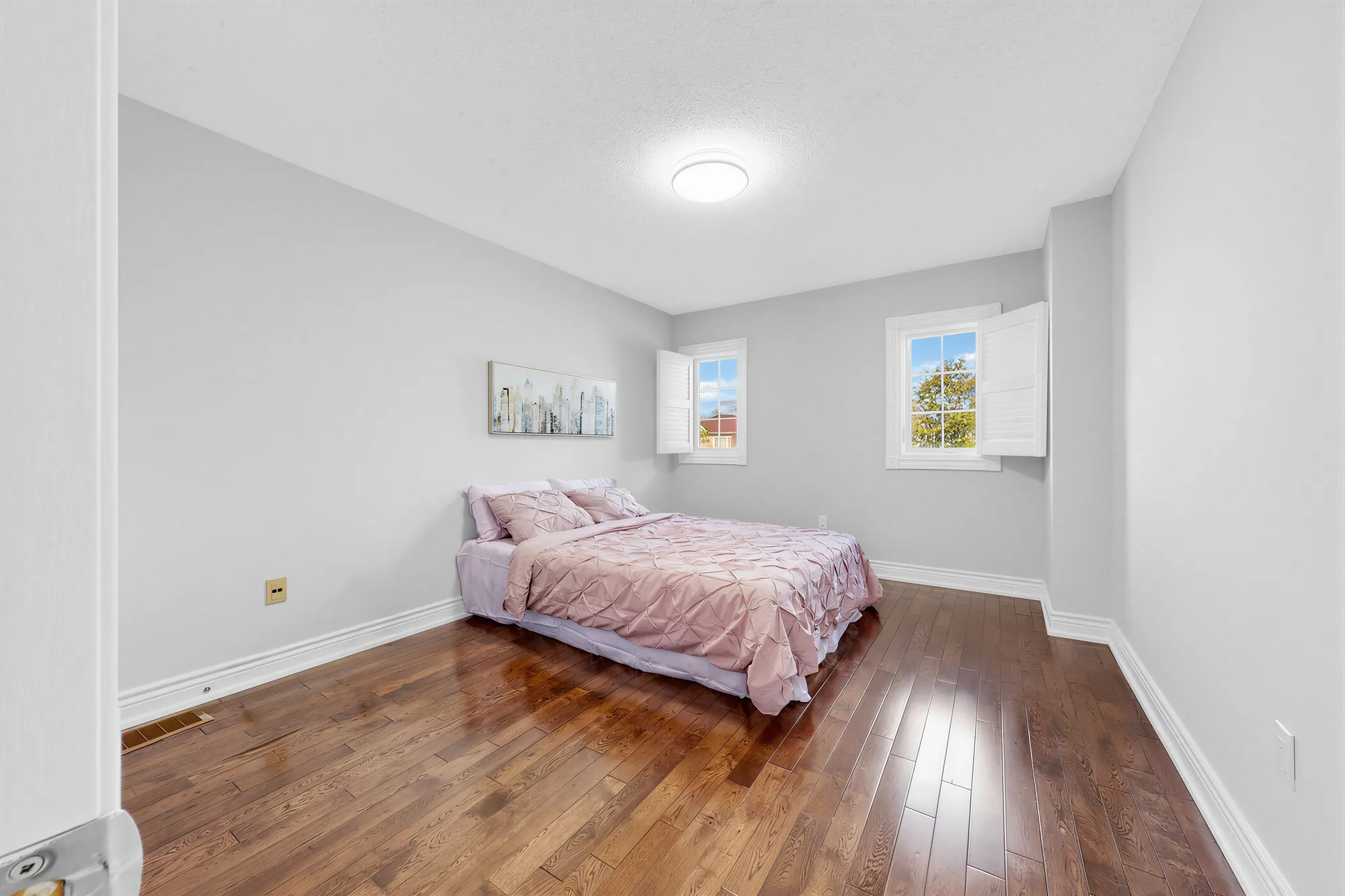 The second front bedroom: two windows with shutters, a bed with a pink cover, hardwood floors