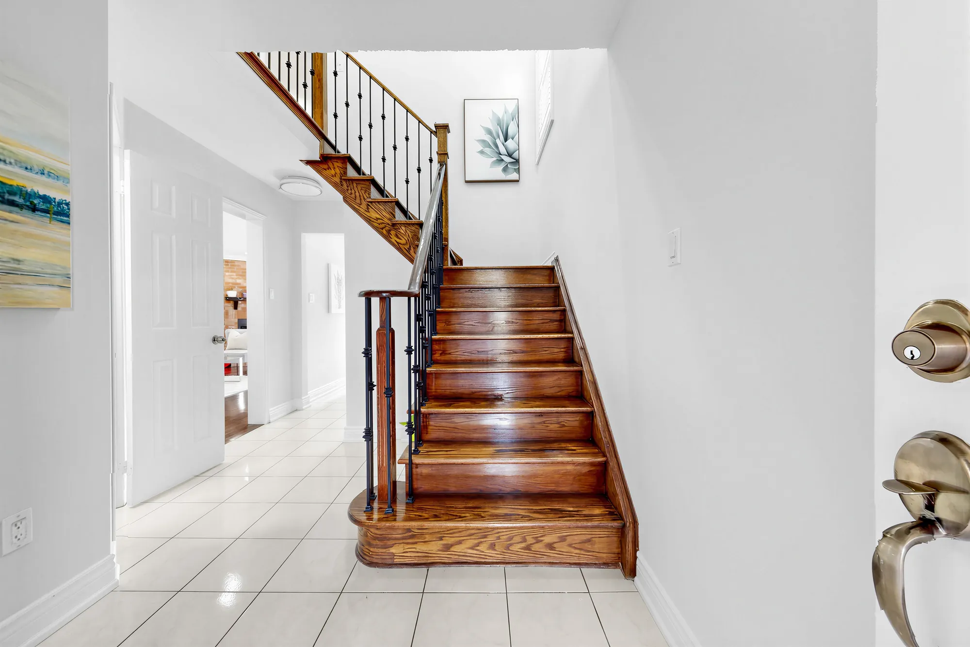 The foyer: a white tile floor, the oak stair with iron balusters rising to the upper hall, white doors to the side