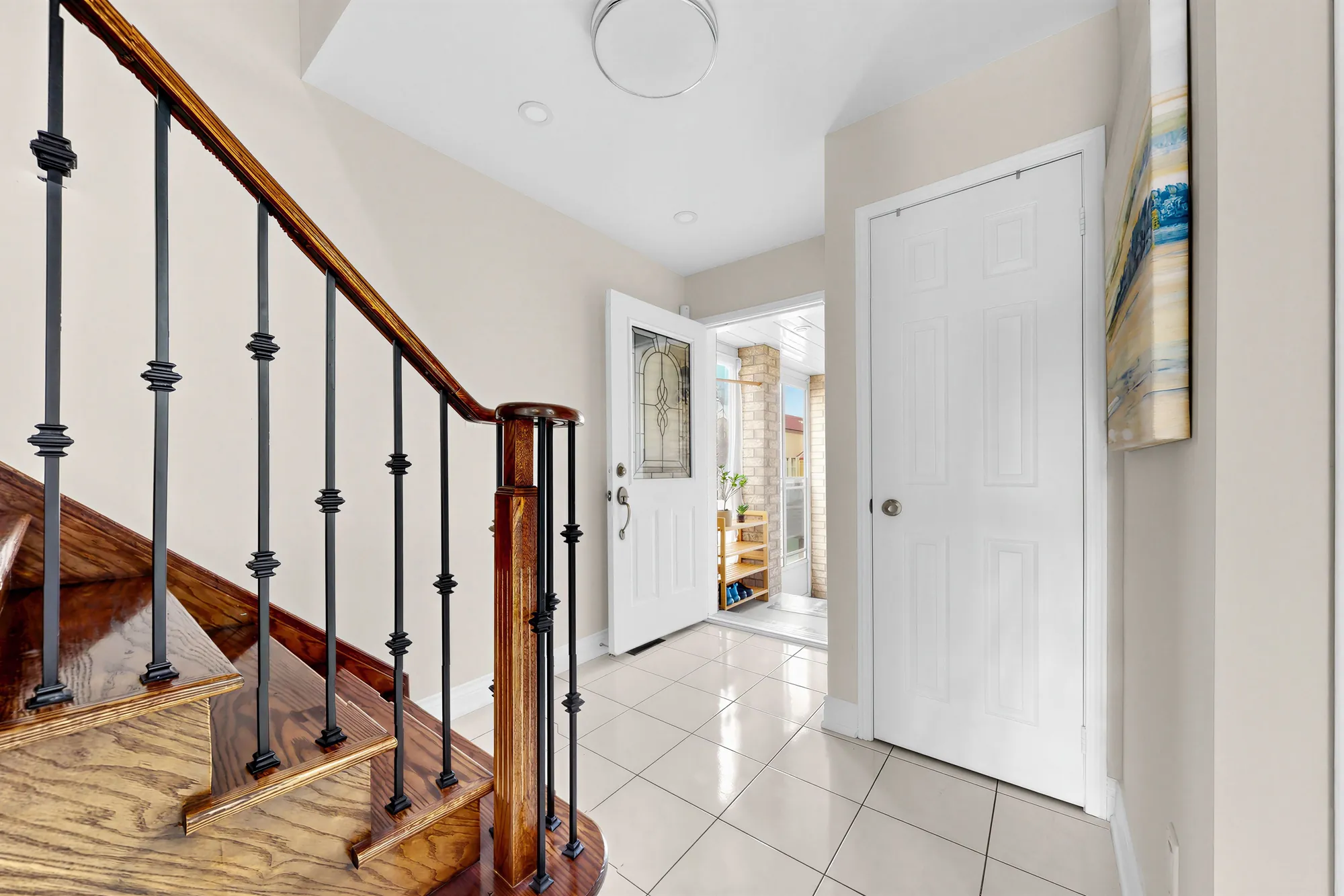 The foyer from the foot of the stair: the house door with a glass insert and the porch beyond, a closet door, the tile floor