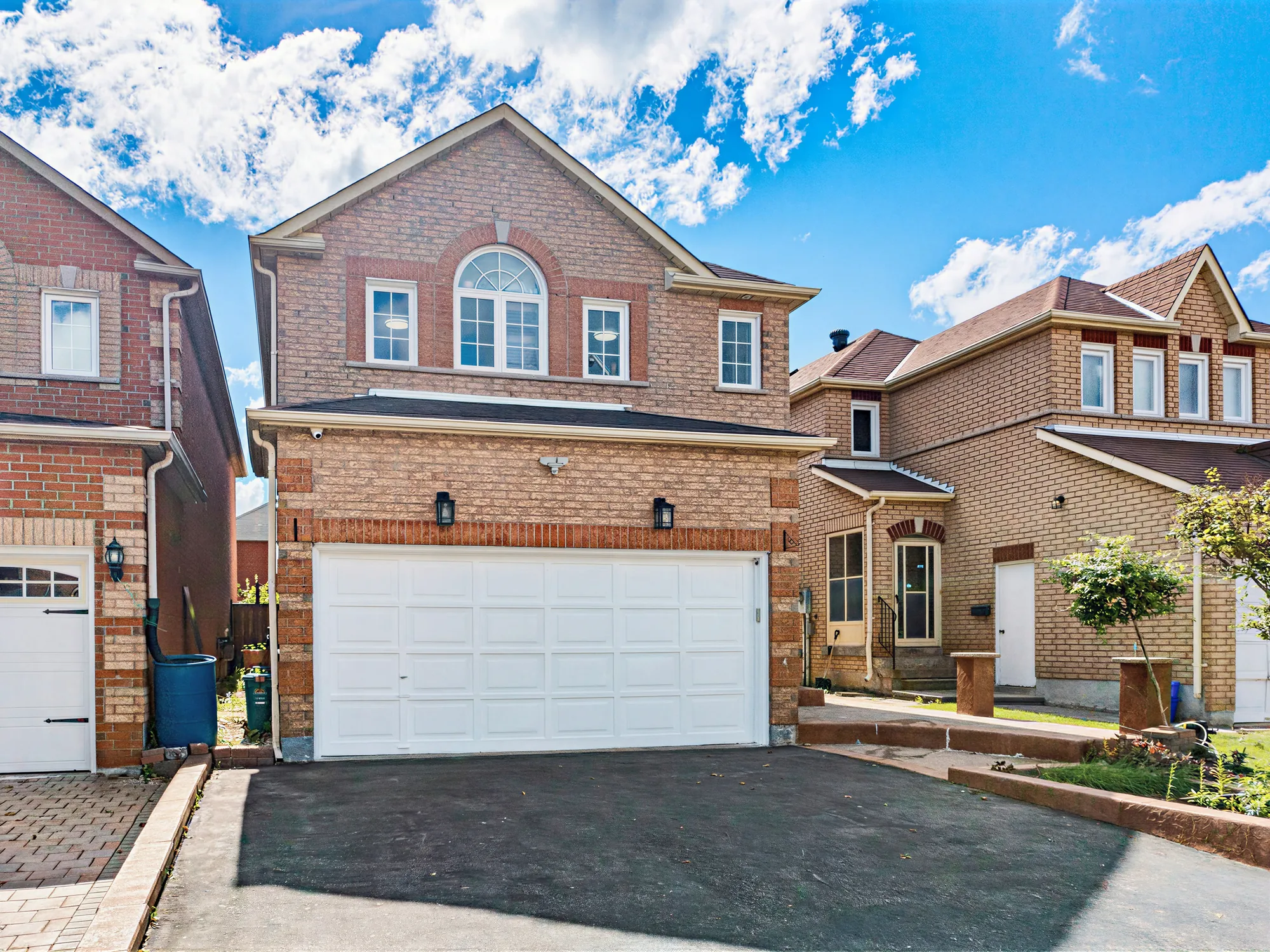 The front from the corner of the drive: the arched window, the garage, the planted bed along the walk, the houses on either side