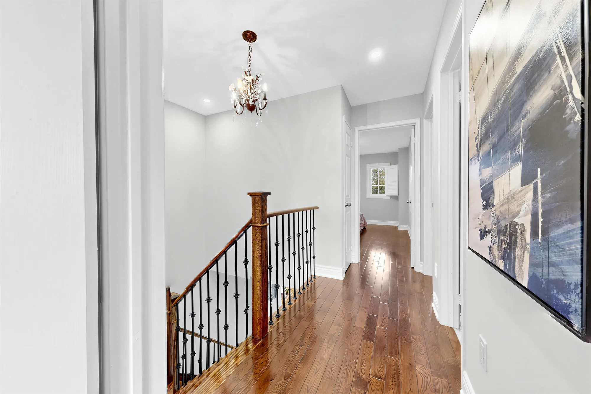The upper hall: hardwood, the stair railing on the left, a small chandelier, a bedroom door at the end