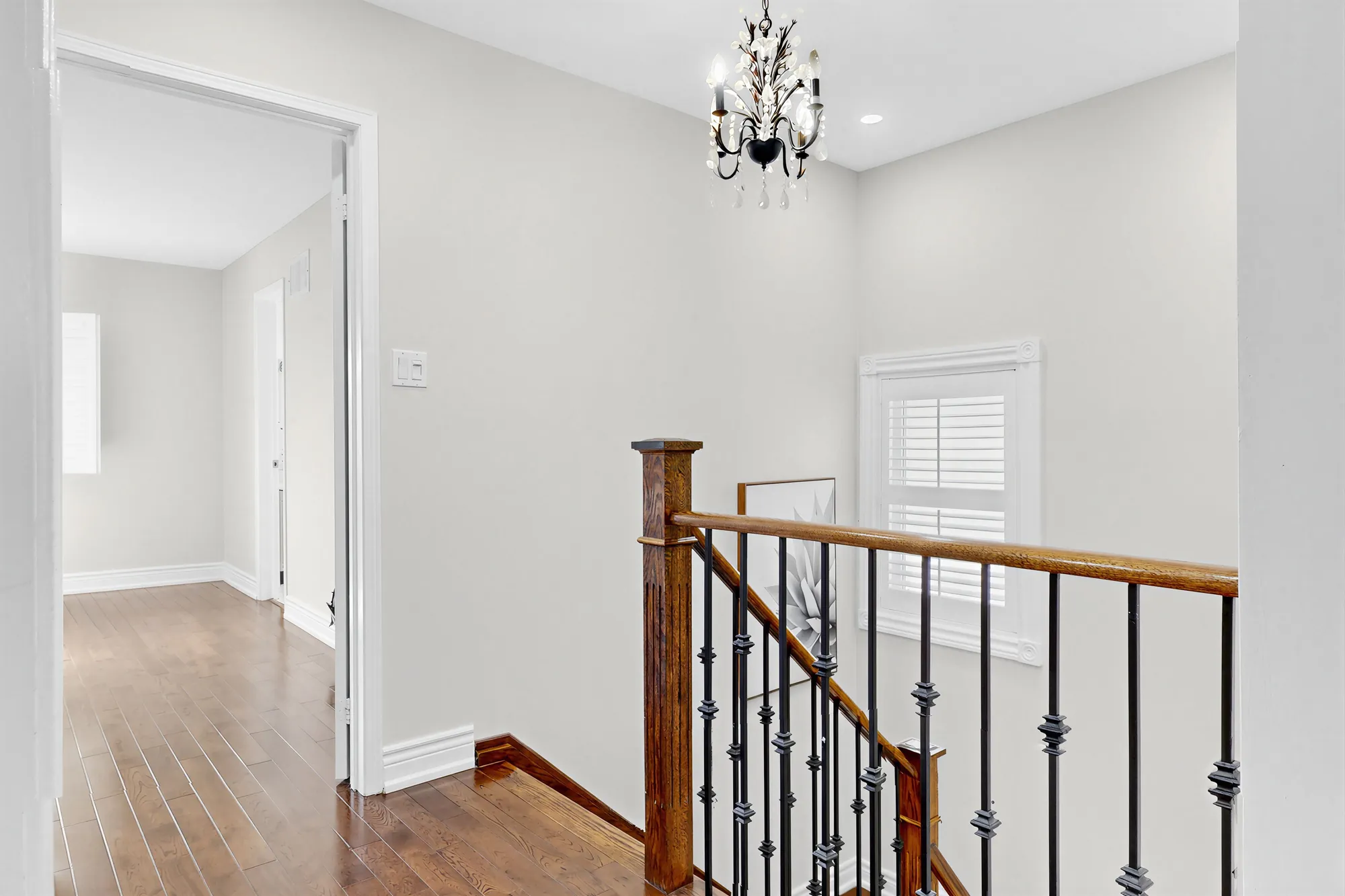 The upper hall above the foyer: the railing, a chandelier, a window with shutters, a bedroom through the door at the left