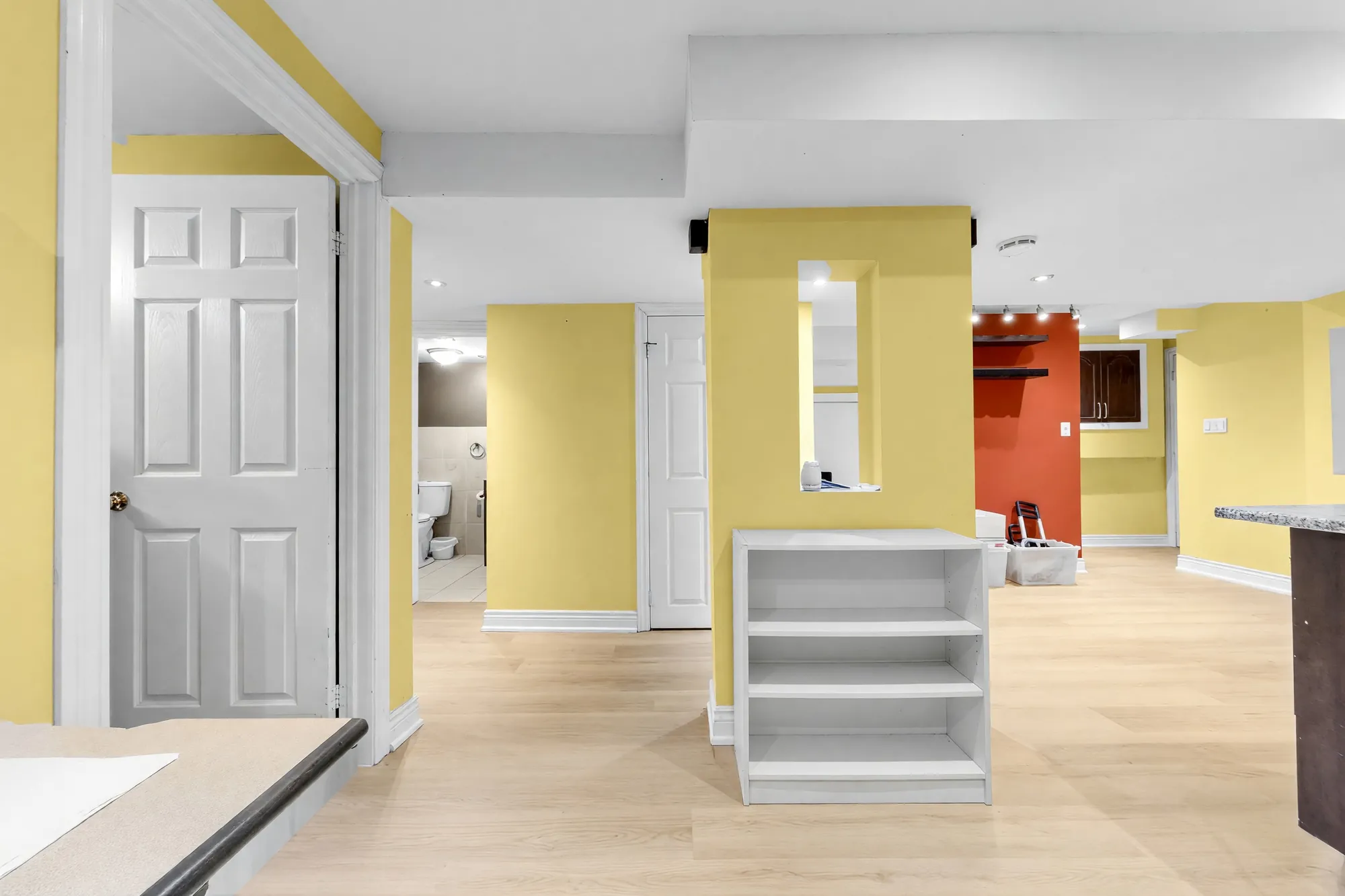 Across the office area shown cleared: a white shelf unit, the yellow column, a door at the left, the bathroom and the red wall beyond