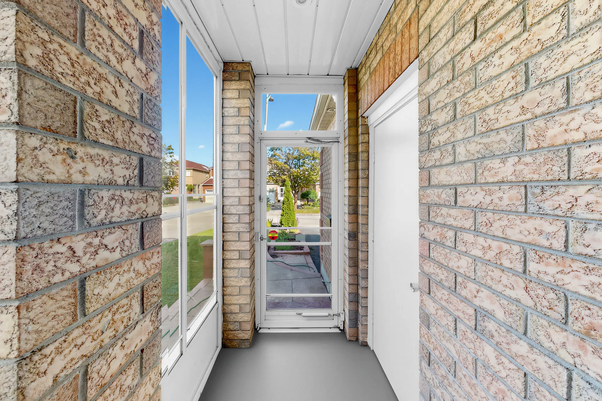 The enclosed porch: brick walls either side, a window along one wall, the glass door at the end to the front of the house