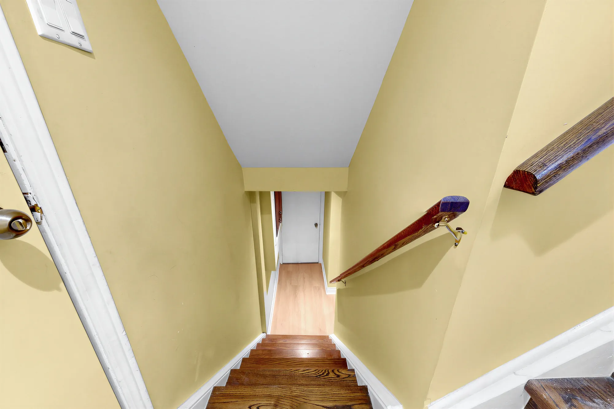The stair down to the lower floor: yellow walls, a wood handrail, a door at the foot