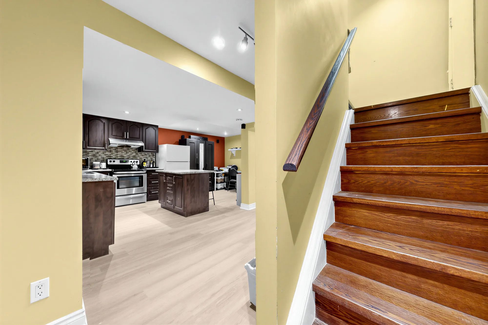 The foot of the stair: the lower-floor kitchen through the opening, its island and range, a red accent wall beyond